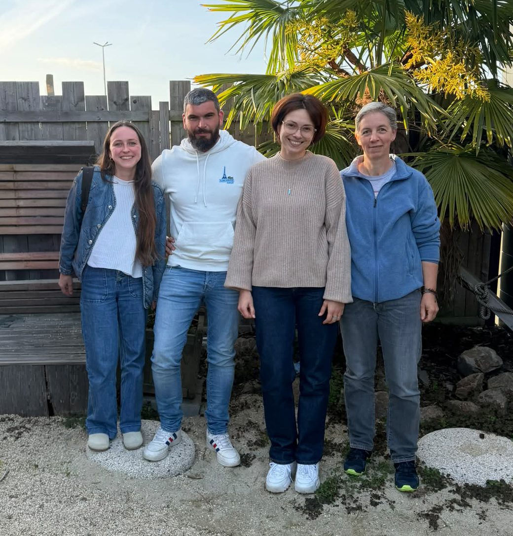 Les quatre membres du collectif debout côte à côte dans un jardin, devant des palmiers.